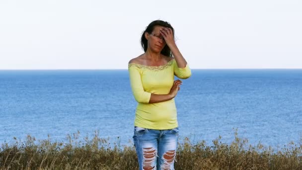 4K. Mujer adulta en blusa amarilla hace pelo en la orilla del mar Día de verano — Vídeo de stock