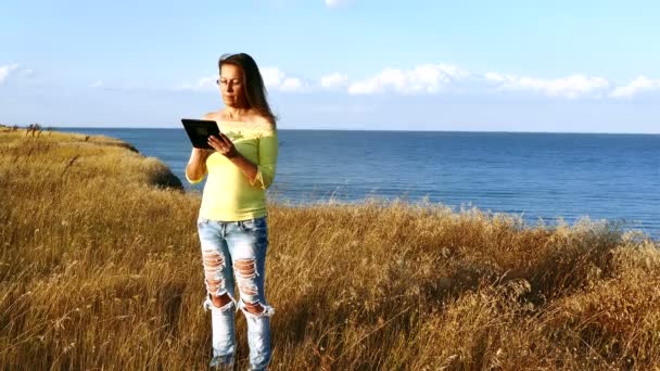 4K.Modern vacaciones y la emoción brillante de la mujer madura armoniosa con la tableta contra el mar — Vídeo de stock