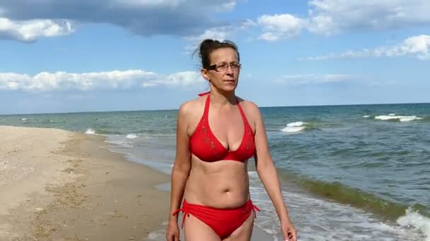 4K. Mujer madura en traje de baño rojo en la playa de mar — Vídeo de stock