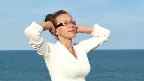 4К. Взрослая женщина в очках с поднятыми руками на поверхности моря — стоковое видео