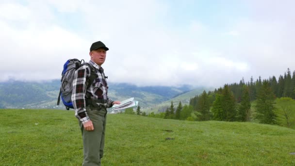 4K. Hombre adulto mochilero turístico en las montañas colina busca camino a través de mapa topográfico — Vídeos de Stock
