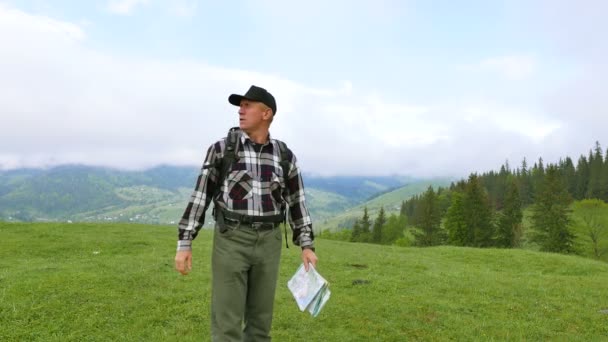 4K. Hombre adulto mochilero turístico en las montañas colina busca camino a través de mapa topográfico — Vídeo de stock