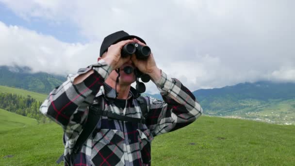 4K.Adult turista mochilero en las montañas mira en los prismáticos y desaparece — Vídeos de Stock