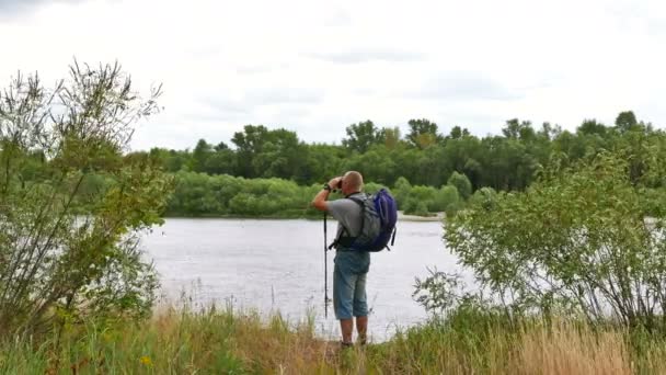 Man toeristische op rivieroever zoekt in de verrekijker en weggaan. 4k 3840 x 2160 — Stockvideo