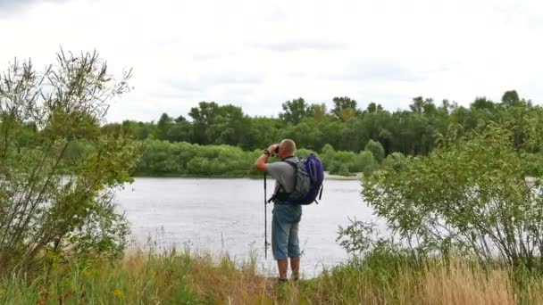 Turistické muž na břehu řeky vypadá v binokulární a jdi pryč. 4k 3840 x 2160 — Stock video