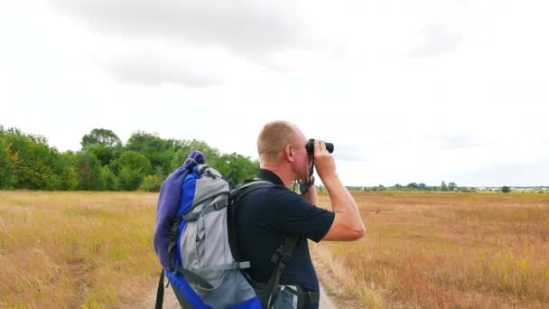 Hombre turista mira en binocular en lugar al aire libre en el campo amarillo. 4K 3840x2160 — Vídeo de stock