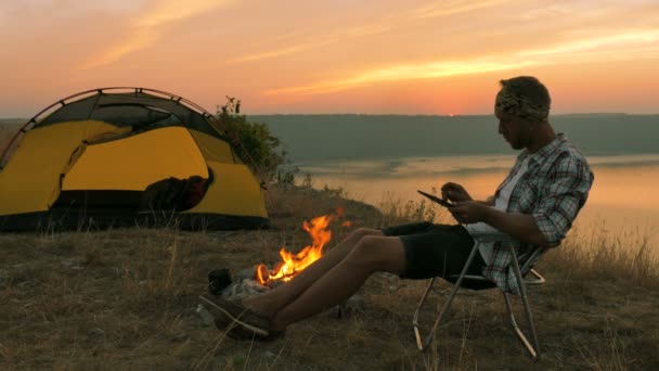 4 k tält, brasa, soluppgång och mannen resenär i soluppgång tid arbete tablett. — Stockvideo