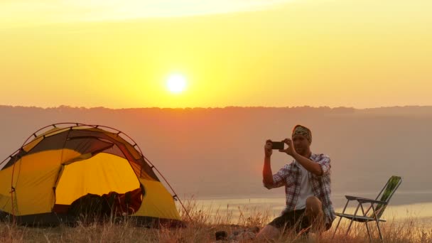 4K Tenda, fogueira, nascer do sol e homem viajante faz selfie por smartphone — Vídeo de Stock