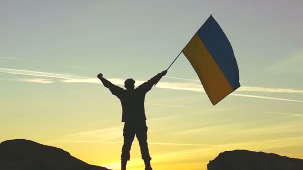 Silhouet van soldaat met Oekraïense vlag tegen oranje hemel. Slow Motion — Stockvideo