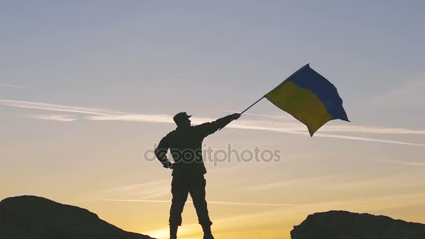 Silhouette de soldat avec drapeau ukrainien contre le ciel orange. Mouvement lent — Video