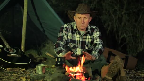 Homem turista aquece as mãos na fogueira. Vida de viagem de outono . — Vídeo de Stock
