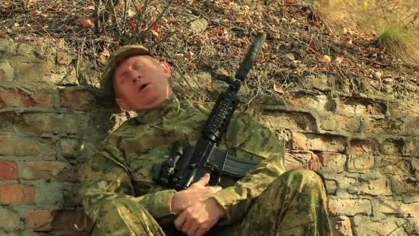 Soldat mit automatischem Gewehr schläft nahe Ziegelmauer — Stockvideo
