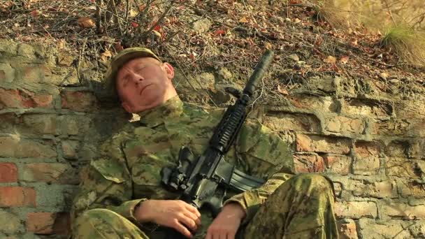 Soldier with automatic rifle  sleep and wake up near  brick wall — Stock Video