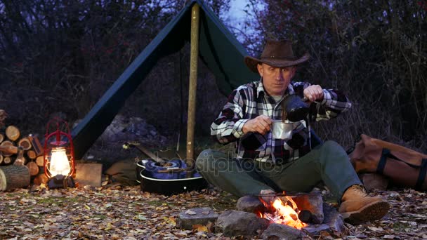 4K.Man en chapeau de cow-boy près de feu de joie faire du café. Vie de voyage d'automne . — Video