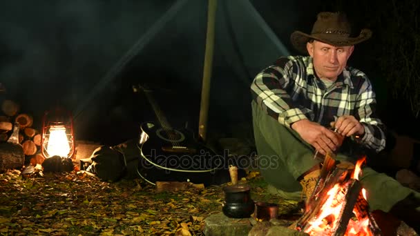 4K. Hombre adulto en sombrero cerca de hoguera bebe alcohol . — Vídeos de Stock