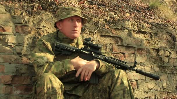 Adult soldat med automatgevär sitta nära tegelvägg — Stockvideo