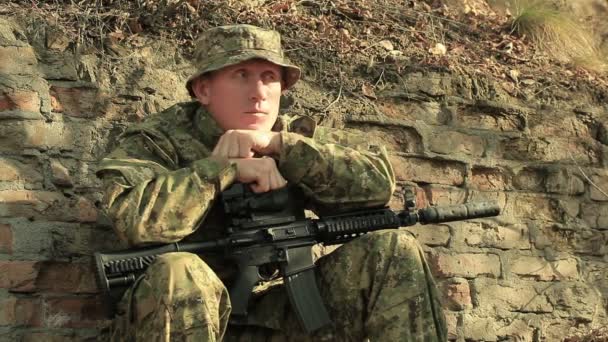 Adult  sad Soldier with automatic rifle    sit near  brick wall — Stock Video