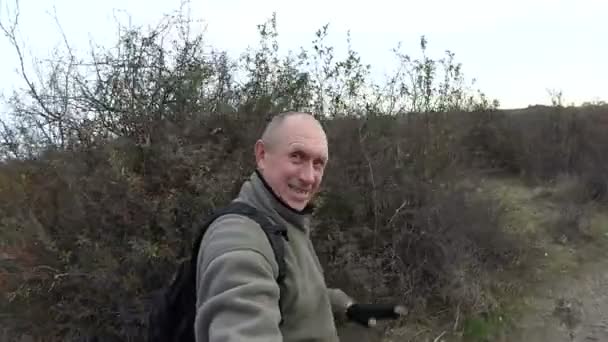 Счастливый человек делает селфи и гуляет по дорожкам среди кустов — стоковое видео