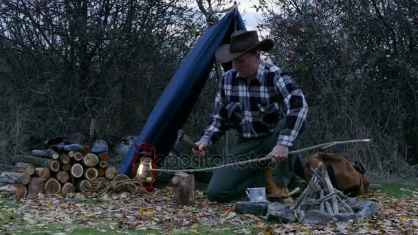 O homem de chapéu de cowboy corta lenha para uma fogueira. Vida de viagem de outono . — Vídeo de Stock