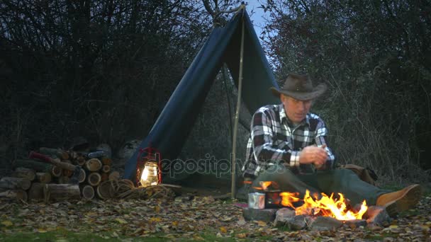 4 k。成年男子在牛仔帽加热的双手靠近篝火。旅行生活. — 图库视频影像