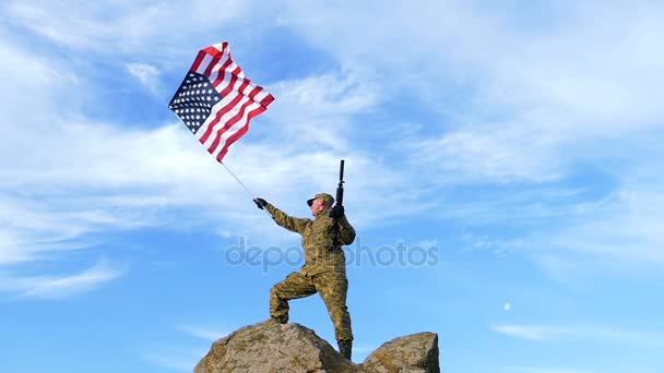 Soldado en la cima de la montaña con rifle automático, y bandera americana. Moción lenta . — Vídeos de Stock