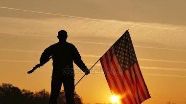 Asansör tüfek kadar asker ve Amerikan bayrağı turuncu gökyüzü karşı tutun. Ağır çekim yakın çekim