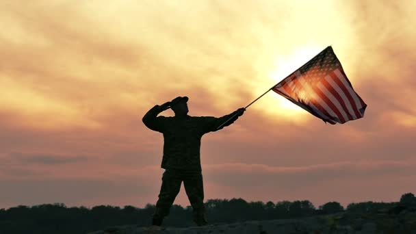 Soldado saúda bandeira americana contra o céu laranja sombrio. Movimento lento — Vídeo de Stock