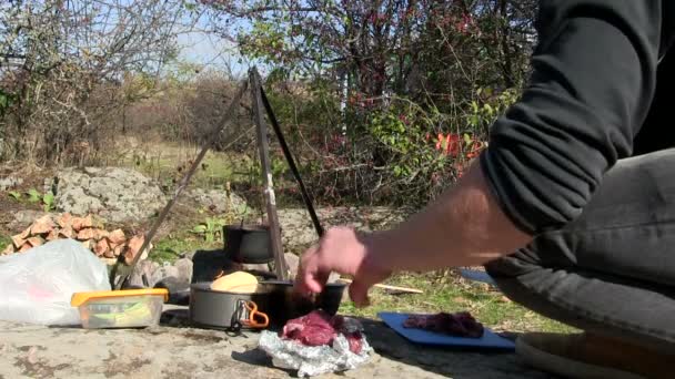 Matlagning utomhus nära brasa. Man skär kött — Stockvideo