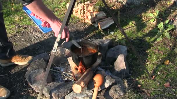 Gotowania żywności na zewnątrz. Mięso umieszcza mięsa w czajnik nad ogniskiem — Wideo stockowe