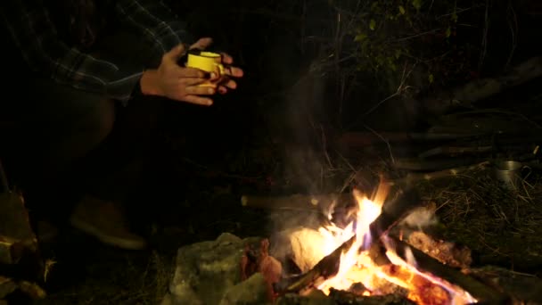 4K.Hombre y taza de café o té en las manos cerca de la hoguera. Vida de viaje de otoño . — Vídeo de stock