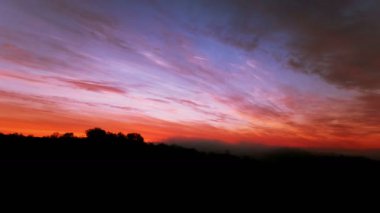  4 K. günbatımı üzerinde kırmızı ve mavi gökyüzü bulutlu ağaçlarda. Zaman atlamalı  