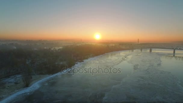 4K Aerial. Зимний пейзаж с замерзшей рекой города и мостом на восходе, закате . — стоковое видео