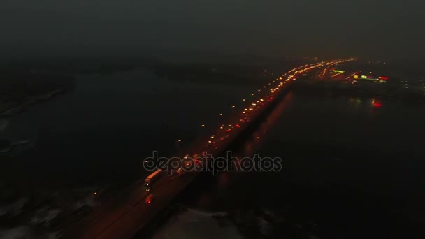 Aérea 4K. Autopista de la ciudad nocturna con tráfico de coches y puente sobre el río, inclinación de la cámara — Vídeo de stock