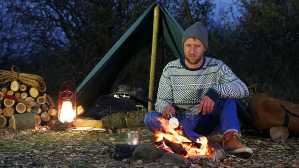 4k . Young man  roasting marshmallows at camp fire. Life on travel — Stock Video