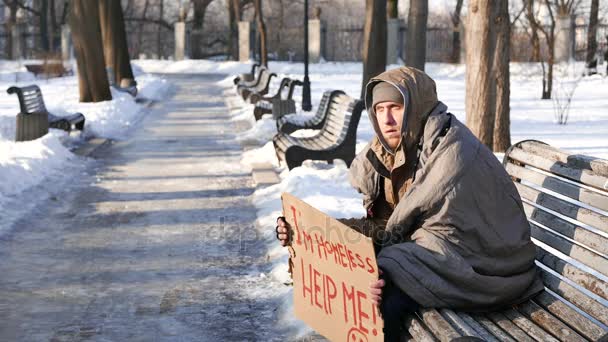 4K.Homeless jovem com papelão sentar e pedir ajuda no parque da cidade de inverno . — Vídeo de Stock