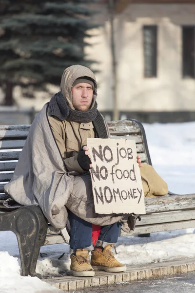 Young   hungry  homeless man with cardboard  in  winter city park — Stock Photo, Image