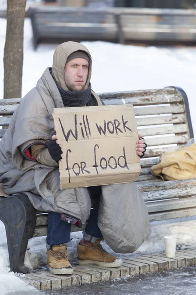 Jonge hongerige dakloze man in winter stadspark op zoek naar baan — Stockfoto