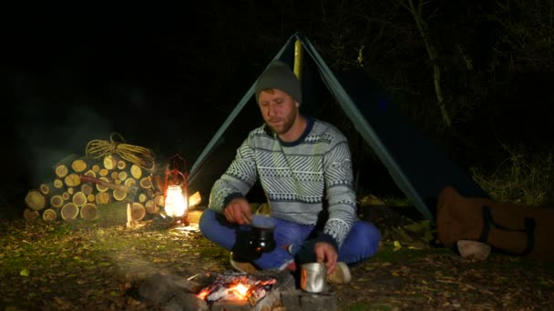 4k . Tourist life. Young man,  traveler, near  campfire drink hot coffee. — Stock Video