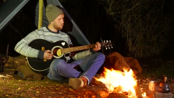 4k. Toeristische leven. Jongeman, reiziger, in de buurt van kampvuur muziek gitaar — Stockvideo