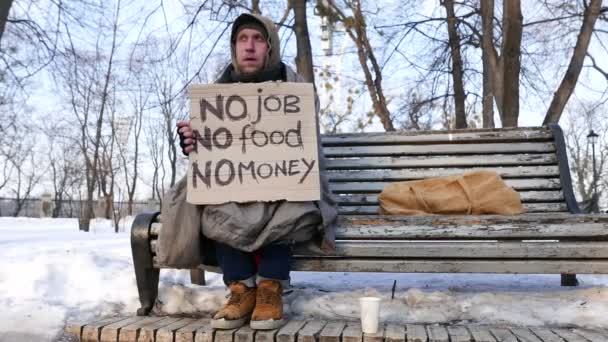 4K. Desempregado. Homem com papelão sentar no banco no parque de inverno. Dolly atirou — Vídeo de Stock