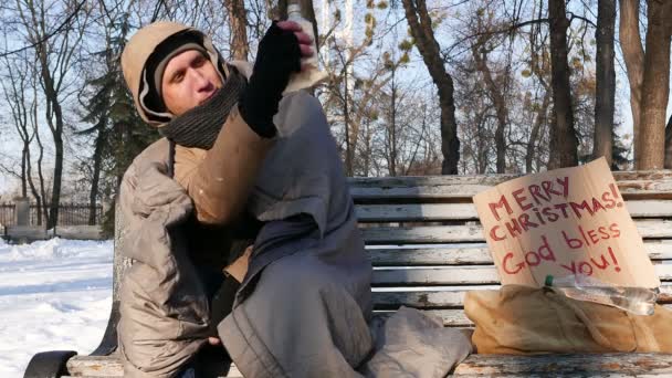 4К. Безработный бездомный. Человек с картонным напитком пьет алкоголь в зимнем парке . — стоковое видео