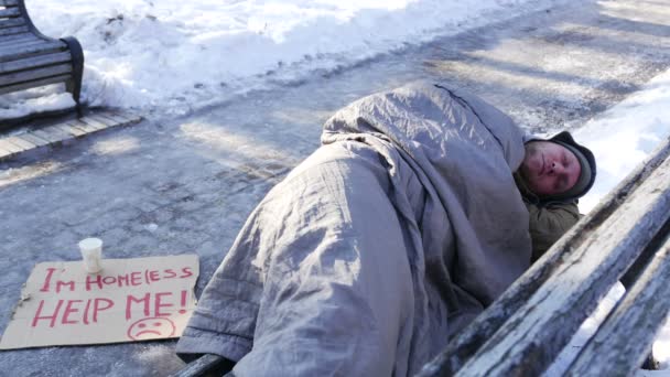 4K. Hombre sin hogar durmiendo en el banco en el parque de invierno . — Vídeos de Stock