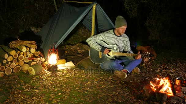 4k. Toeristische muziek leven. Man reiziger, in de buurt van kampvuur en tent tunes-gitaar. — Stockvideo