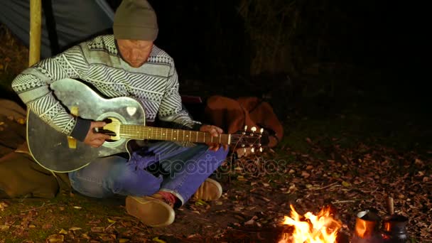 4K. Vida musical turística. Homem viajante, perto de fogueira e tenda melodias guitarra . — Vídeo de Stock