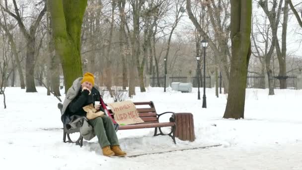 4K. Homeless man in cold winter city park eat burger and drink coffee. Abordagem do foco — Vídeo de Stock