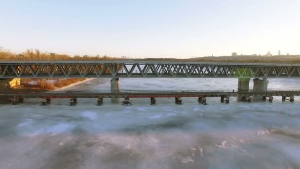 4K Aerial. Летите вниз к замерзшей зимней реке в пригороде города, мост, солнечный день — стоковое видео