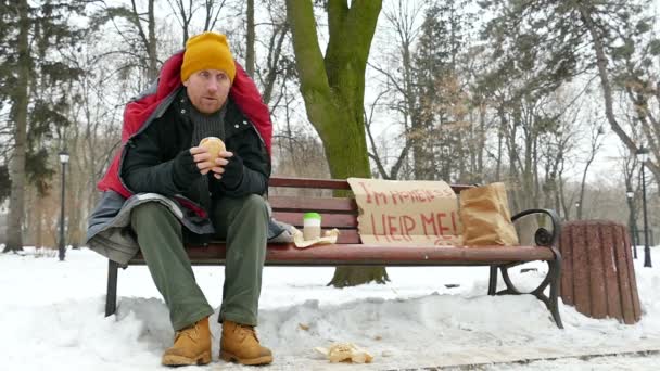 Zpomalený pohyb. Bezdomovec v chladných zimních městského parku s burger. — Stock video
