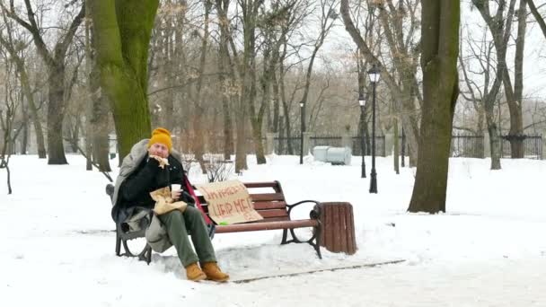 4 k. 食べるハンバーガー、冬公園でホームレスの男性のディナー。フォーカスのアプローチ — ストック動画
