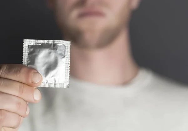 La mano del hombre joven sostiene el embalaje de los preservativos. Imagen recortada — Foto de Stock