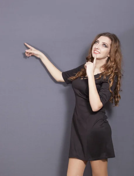 Atractiva joven en vestido negro sostiene el dedo hacia arriba —  Fotos de Stock